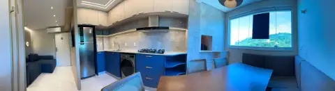 Vista panorâmica de cozinha planejada em azul com bancada integrada à sala de jantar