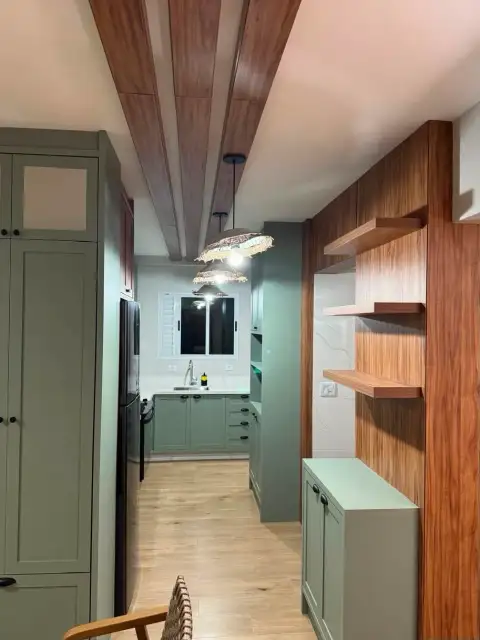 Corredor de cozinha planejada em verde-oliva com viga aparente em madeira e luminárias pendentes