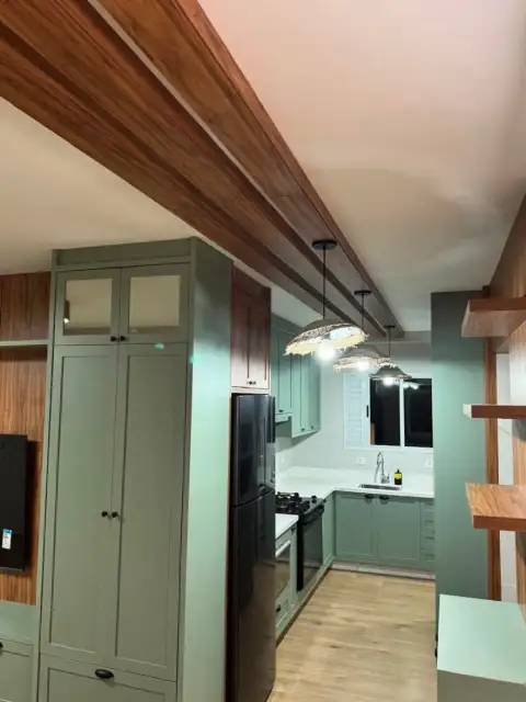 Cozinha planejada verde-oliva com viga de madeira e eletrodomésticos pretos embutidos