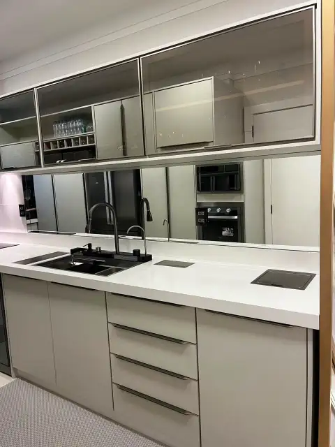 Bancada de cozinha com cooktop, cuba e espelho refletindo eletrodomésticos