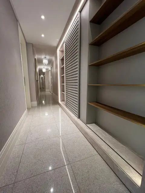 Corredor com prateleiras em madeira, porta perfurada e lustre de cristais ao fundo