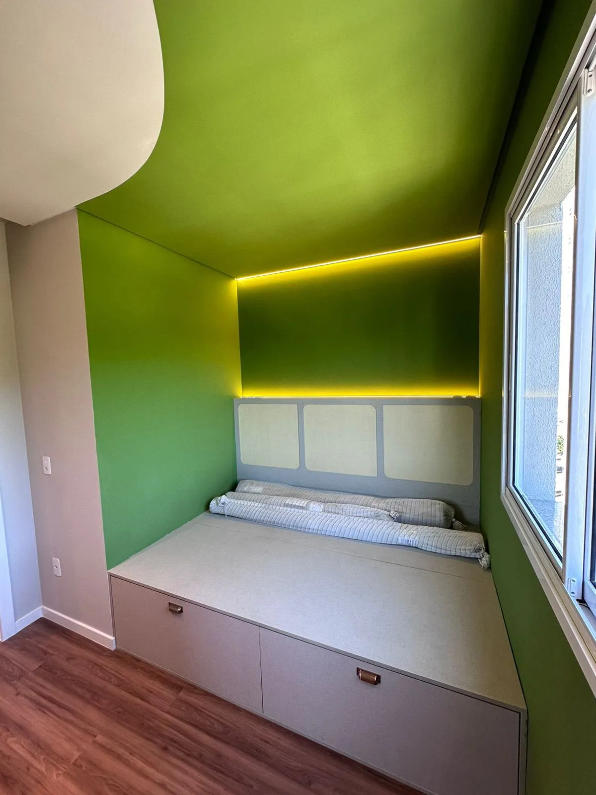 Quarto com parede verde, cabeceira em marcenaria com iluminação em LED âmbar