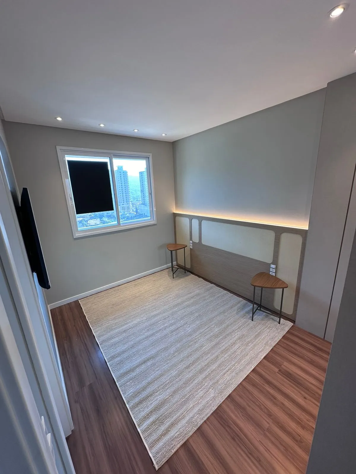 Quarto vazio com tapete, piso de madeira e cabeceira integrada em marcenaria
