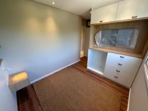 Quarto com painel de TV embutido, cômoda com puxadores dourados e espelho oval