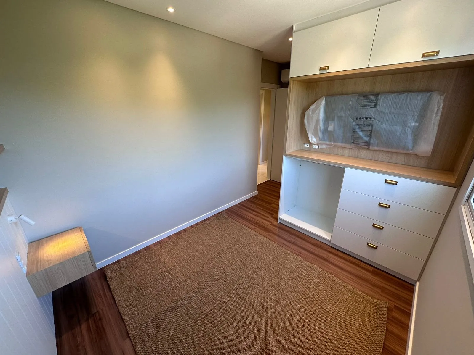 Quarto com painel de TV embutido, cômoda com puxadores dourados e espelho oval
