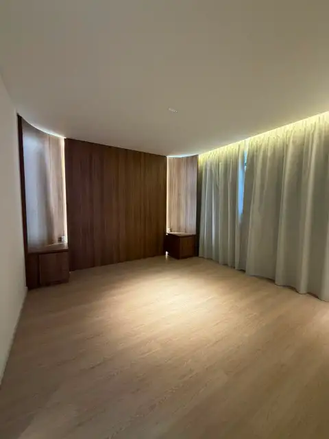 Quarto com painel de marcenaria em tom grafite, cortinas longas e criados-mudos