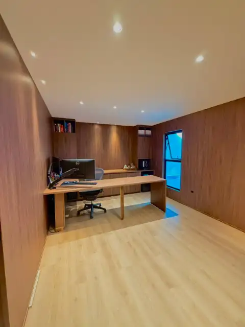 Home office com marcenaria em madeira escura, mesa integrada e estantes