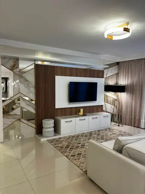 Sala de estar com painel de TV em madeira e mármore, cortinas e luminária de piso