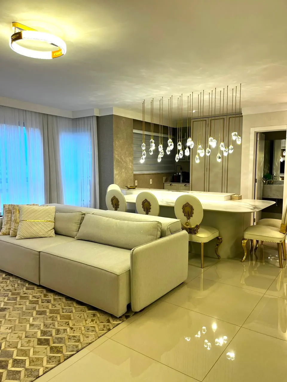Sala de estar com bancada gourmet, lustre de cristais e poltronas estofadas douradas