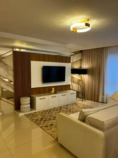 Sala de estar com painel de TV em madeira e mármore sob luminária circular dourada