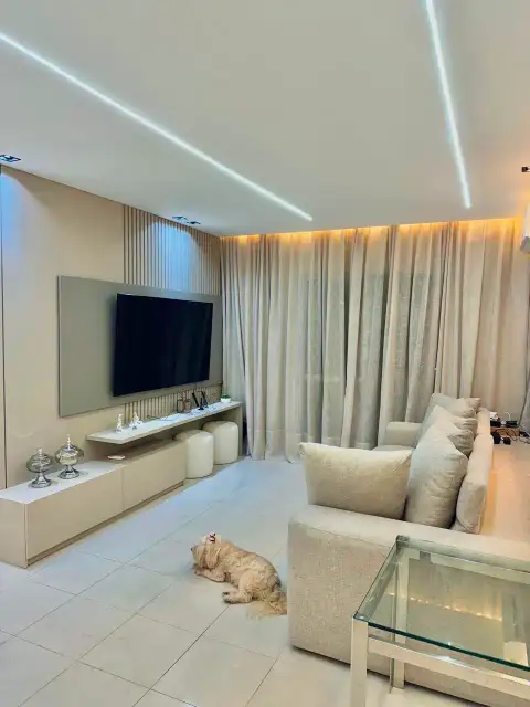 Sala de estar com painel ripado, cortina de linho e iluminação indireta em cove