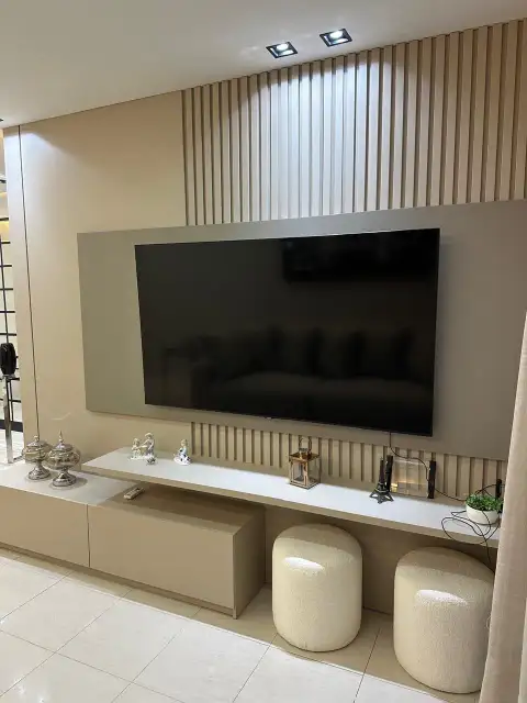 Sala de estar com painel de TV bege, puffs boucle e prateleira flutuante